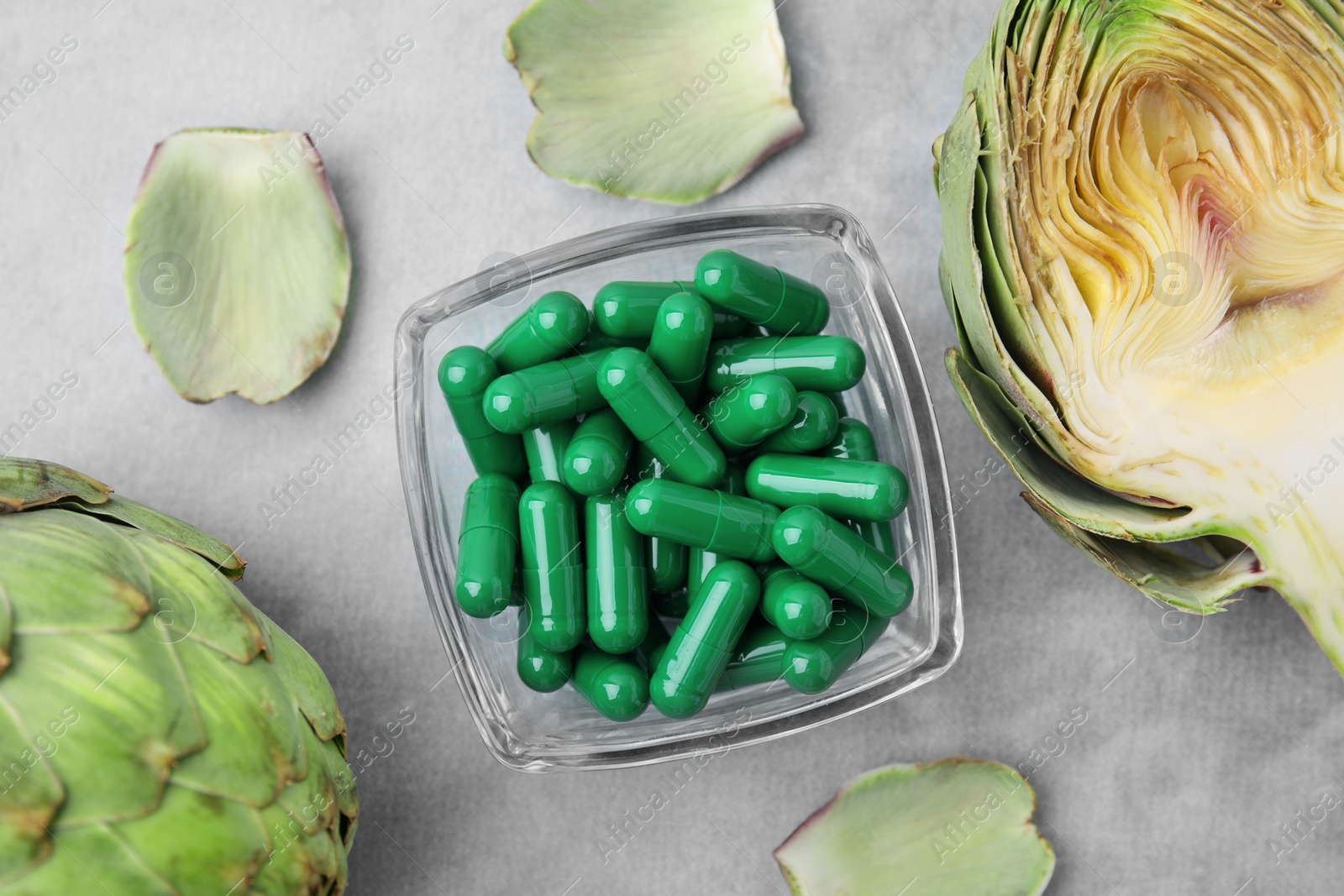 Photo of Bowl with pills and fresh artichokes on grey table, flat lay