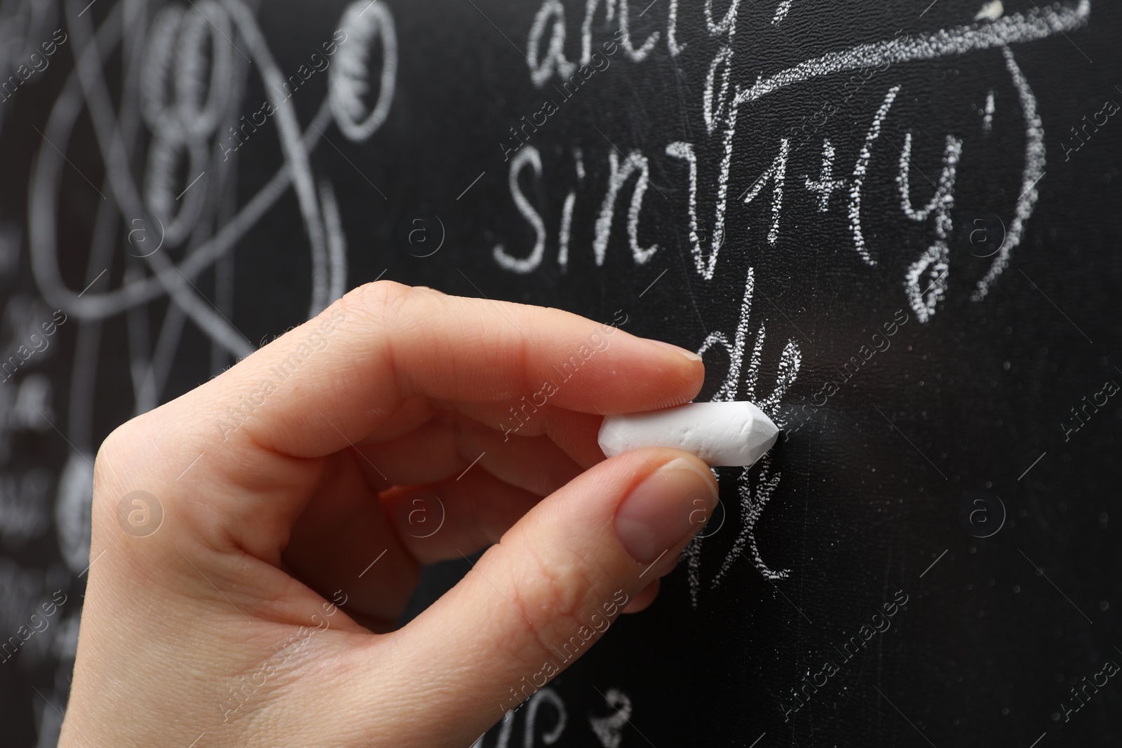 Photo of Teacher writing math formulas with chalk on blackboard, closeup