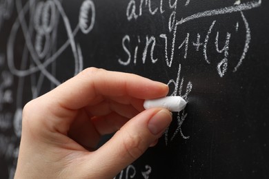 Teacher writing math formulas with chalk on blackboard, closeup