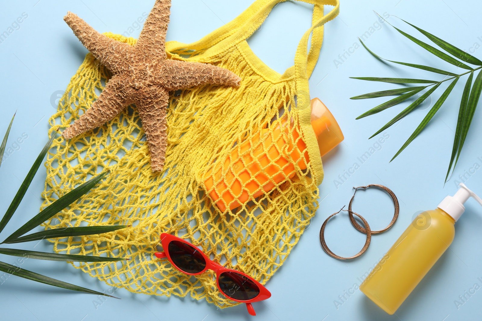 Photo of String bag, different beach accessories and palm leaves on light blue background, flat lay