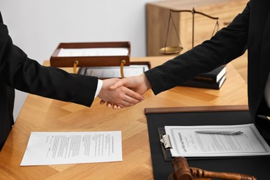 Photo of Notary shaking hands with client at wooden table in office, closeup