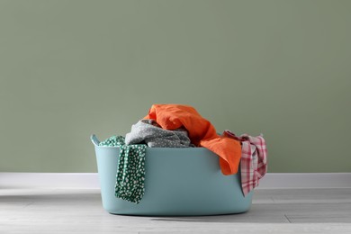 Photo of Laundry basket with clothes near light green wall indoors