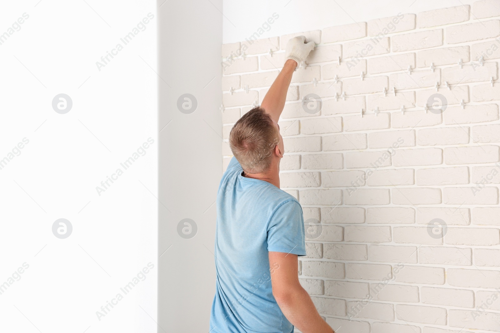 Photo of Worker installing new white decorative bricks on wall indoors