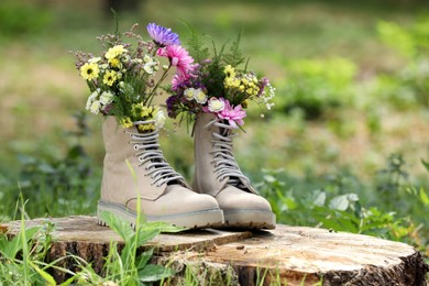 Photo of Beautiful flowers in boots on stump outdoors, space for text
