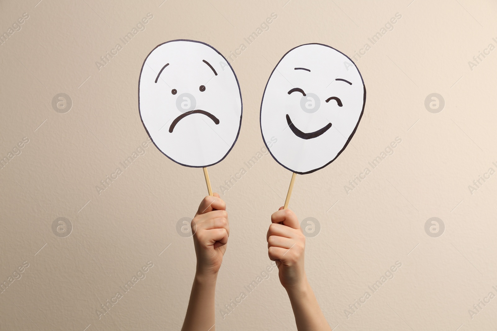 Photo of Woman with sad and happy paper faces on beige background, closeup