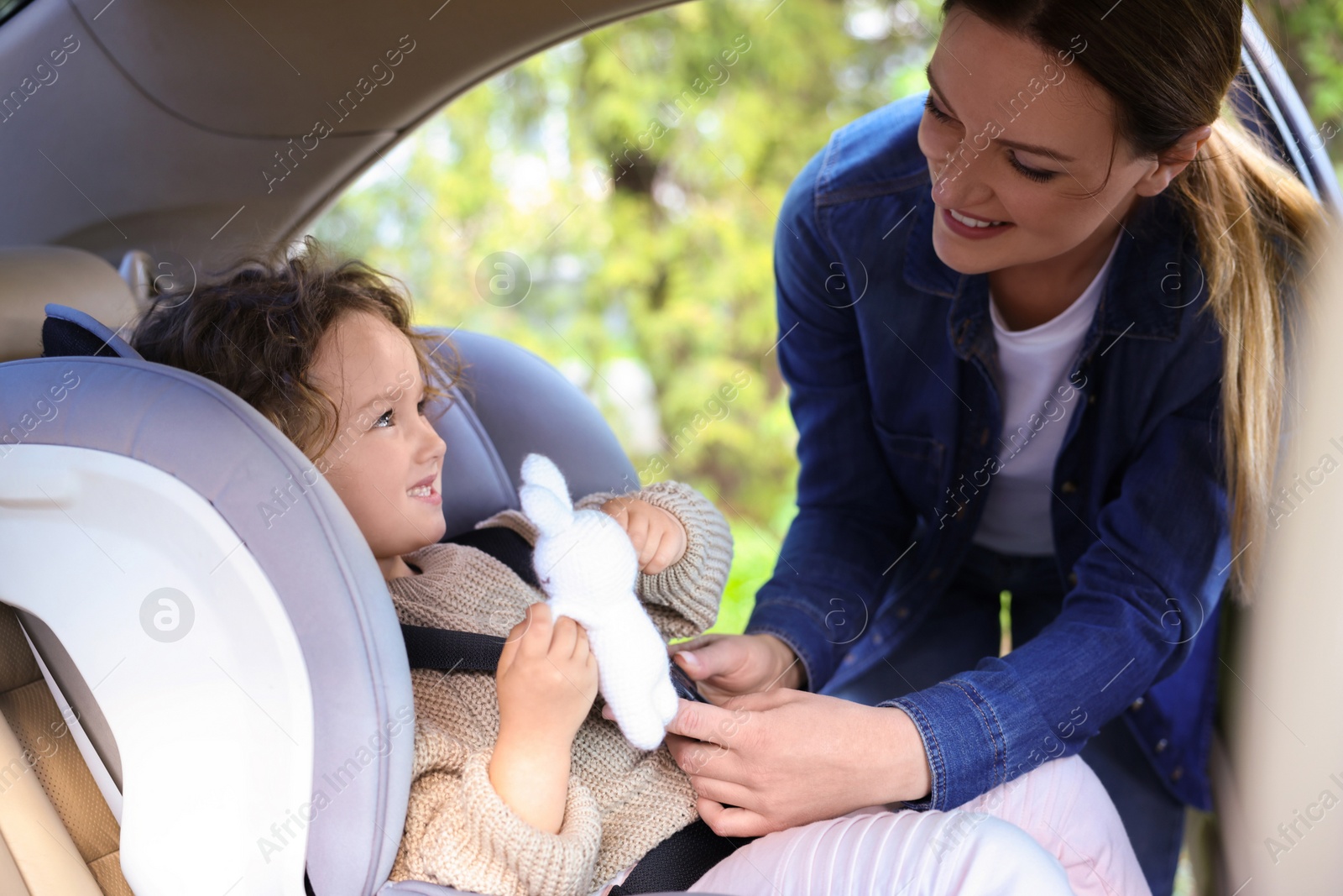 Photo of Mother fastening her daughter in child safety seat inside car