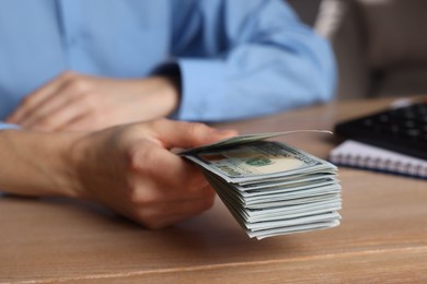 Money exchange. Woman holding dollar banknotes at wooden table, closeup