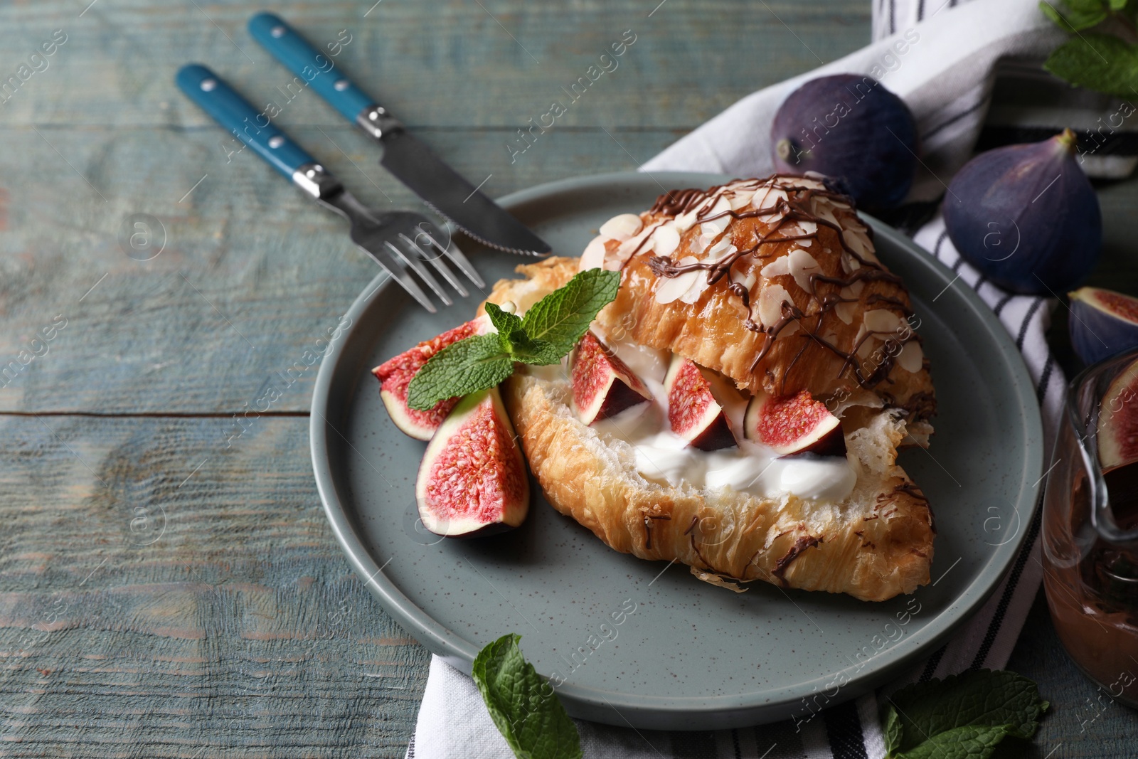 Photo of Delicious croissant with figs and cream served on light blue wooden table