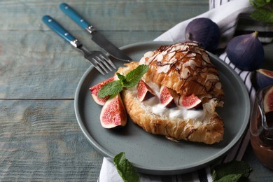 Delicious croissant with figs and cream served on light blue wooden table