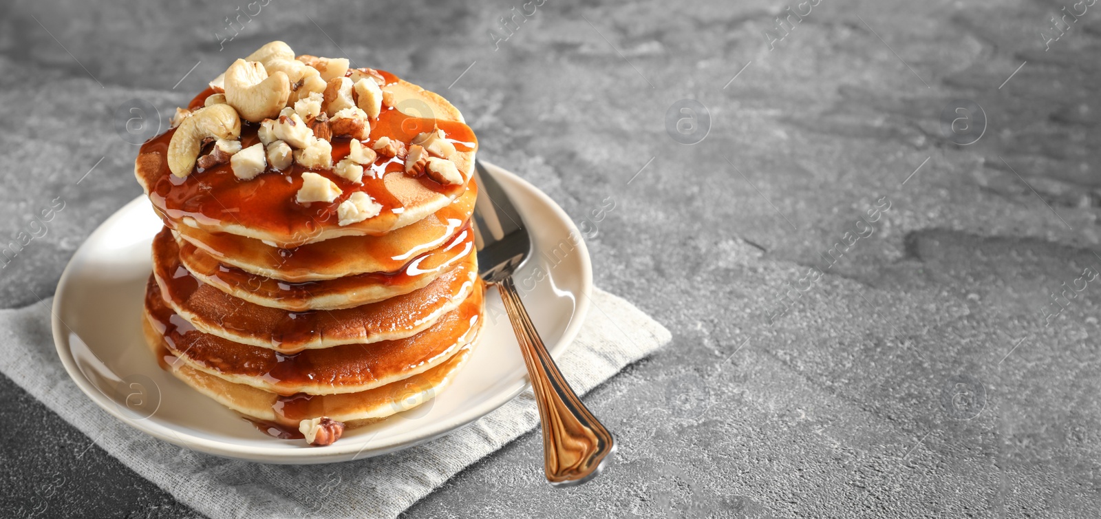 Image of Stack of tasty pancakes with nuts and syrup on table, space for text. Banner design