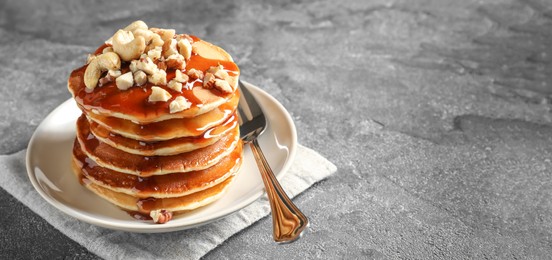 Stack of tasty pancakes with nuts and syrup on table, space for text. Banner design