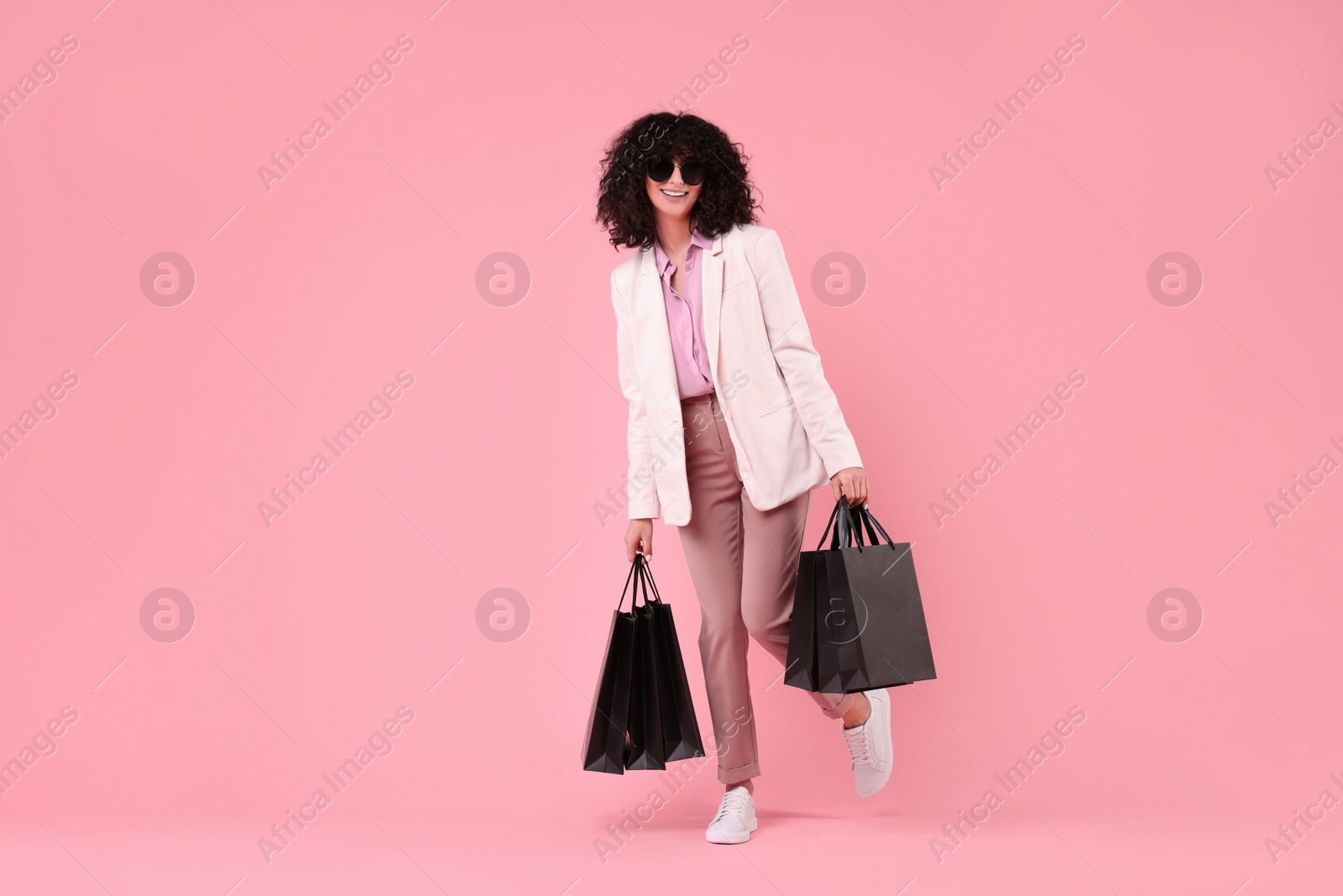 Photo of Happy young woman with shopping bags and stylish sunglasses on pink background. Space for text