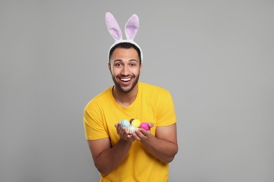 Photo of Happy African American man in bunny ears headband with Easter eggs on gray background