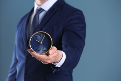 Businessman holding alarm clock on color background. Time concept