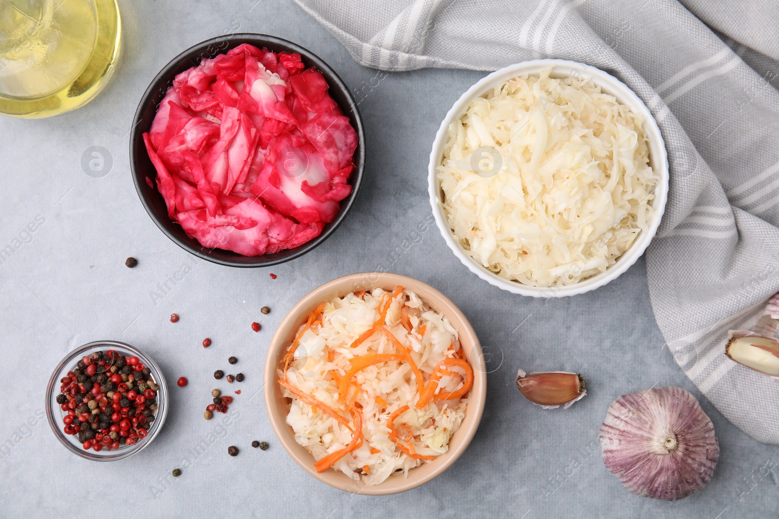 Photo of Delicious sauerkraut prepared according to different recipes and spices on light gray table, flat lay