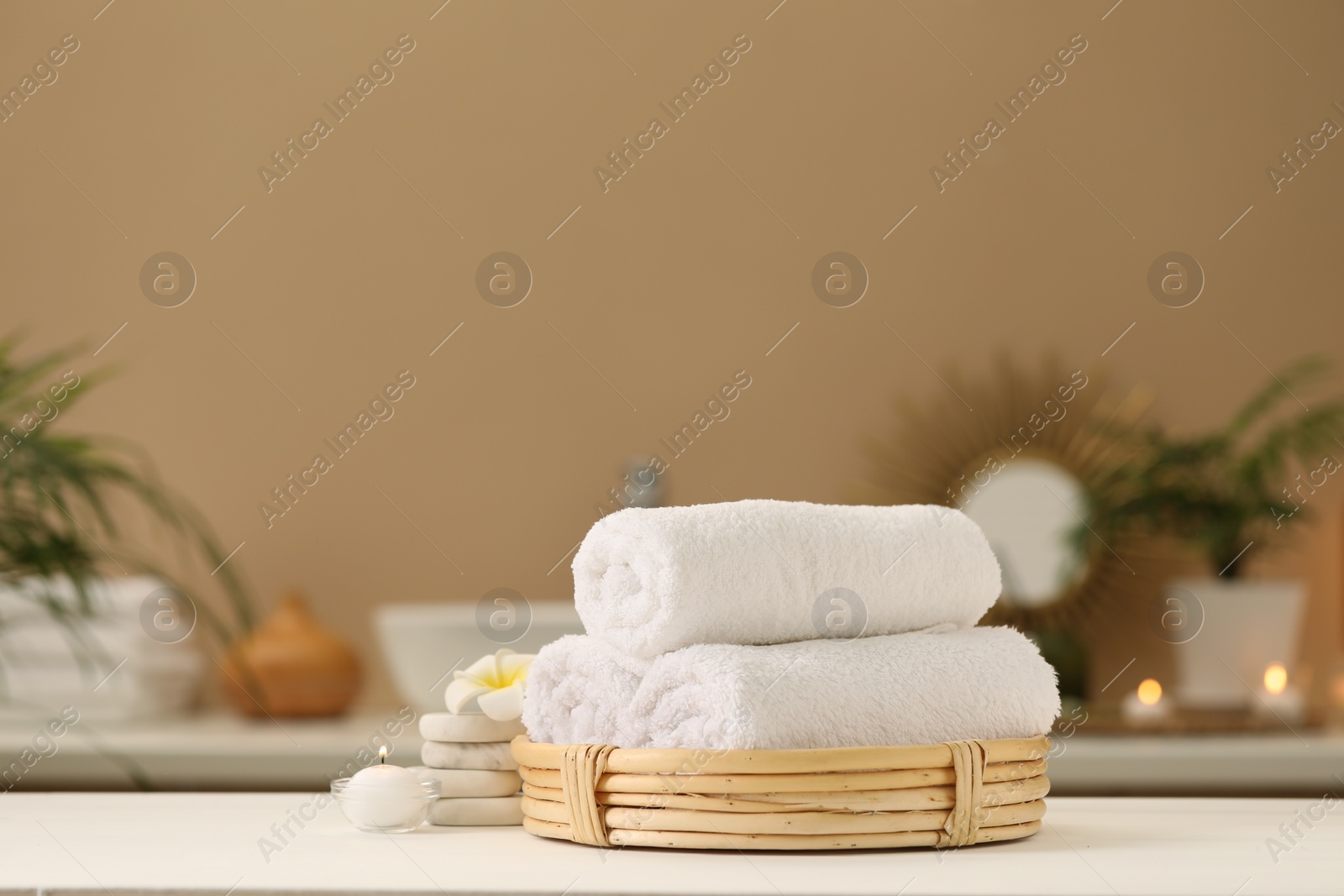 Photo of Spa composition. Rolled towels, massage stones, burning candle and plumeria flower on table. Space for text