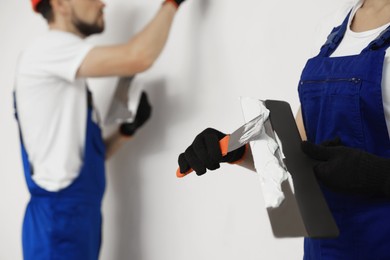Photo of Professional workers with putty knives near wall, closeup