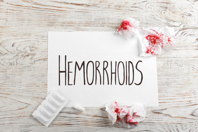 Photo of Sheet of paper with word HEMORRHOIDS on white wooden table, flat lay
