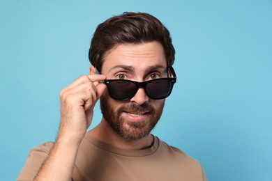 Photo of Portrait of bearded man with stylish sunglasses on light blue background. Space for text