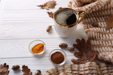 Photo of Cup of hot drink, spices, leaves and knitted scarf on white wooden table. Cozy autumn atmosphere