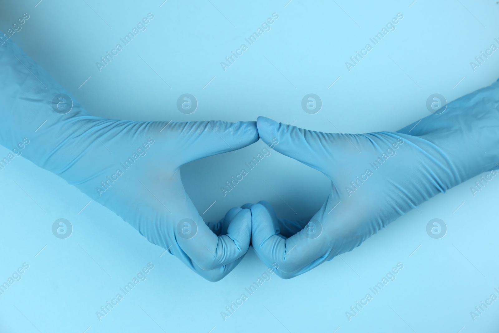 Photo of Person in medical gloves making heart with hands on light blue background, top view