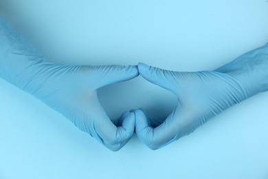 Person in medical gloves making heart with hands on light blue background, top view