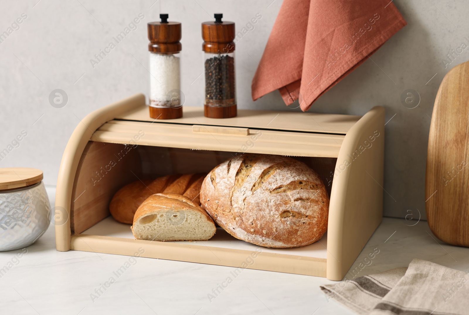 Photo of Wooden bread basket with freshly baked loaves on white marble table in kitchen