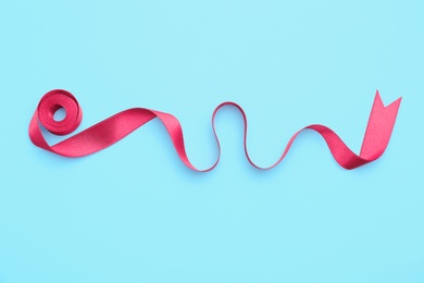 Simple pink ribbon on color background, top view