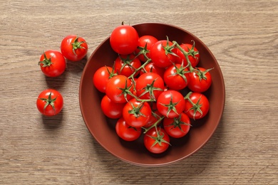 Plate with fresh cherry tomatoes on wooden background, top view