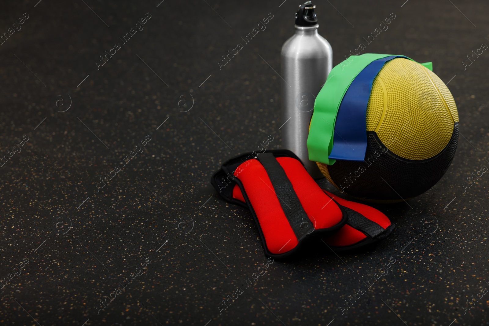 Photo of Medicine ball, bottle, weighting agents and elastic bands on floor, space for text