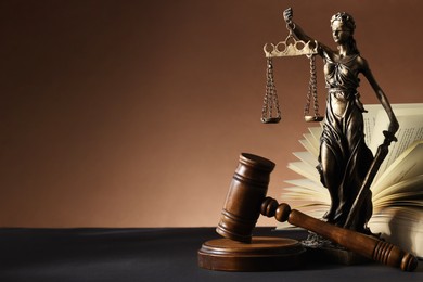 Photo of Statue of Lady Justice near gavel and open book on dark table, space for text. Symbol of fair treatment under law