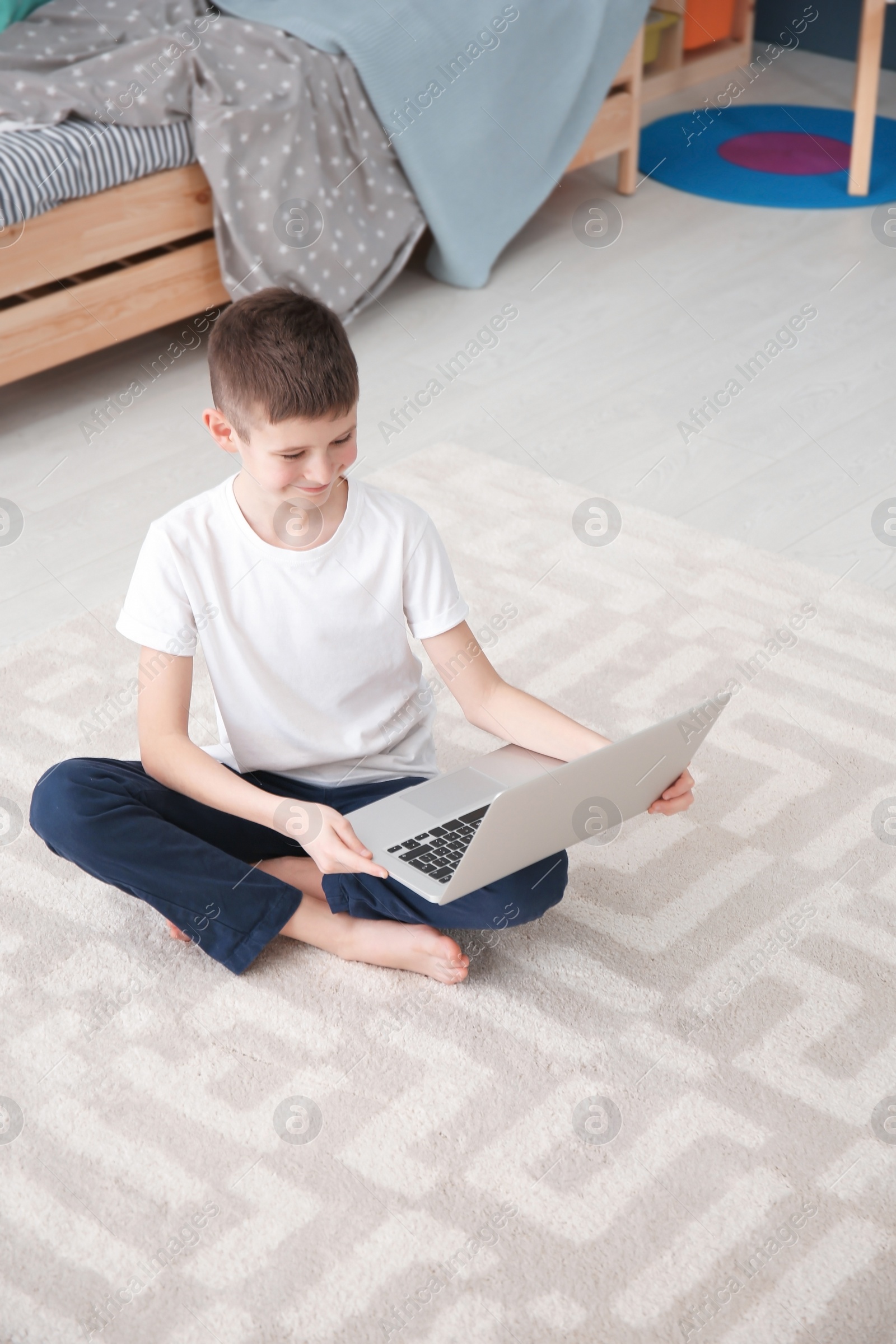 Photo of Happy boy with laptop sitting on cozy carpet at home