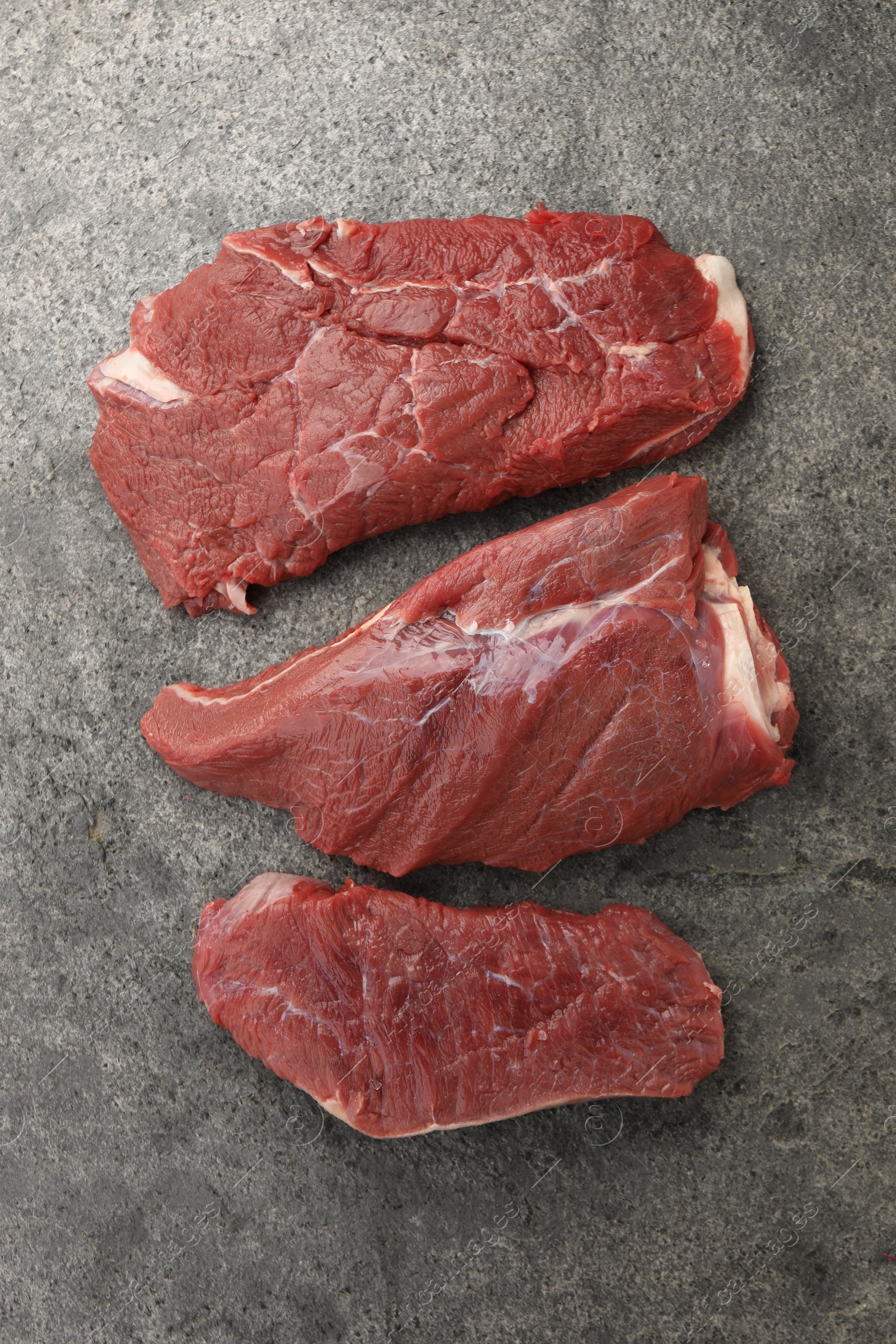 Photo of Pieces of raw beef meat on grey table, flat lay