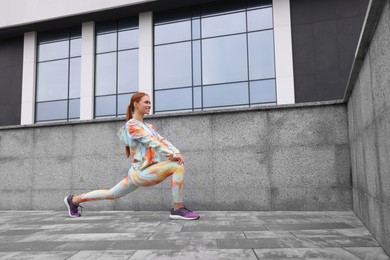 Beautiful woman in gym clothes doing exercises on street, space for text