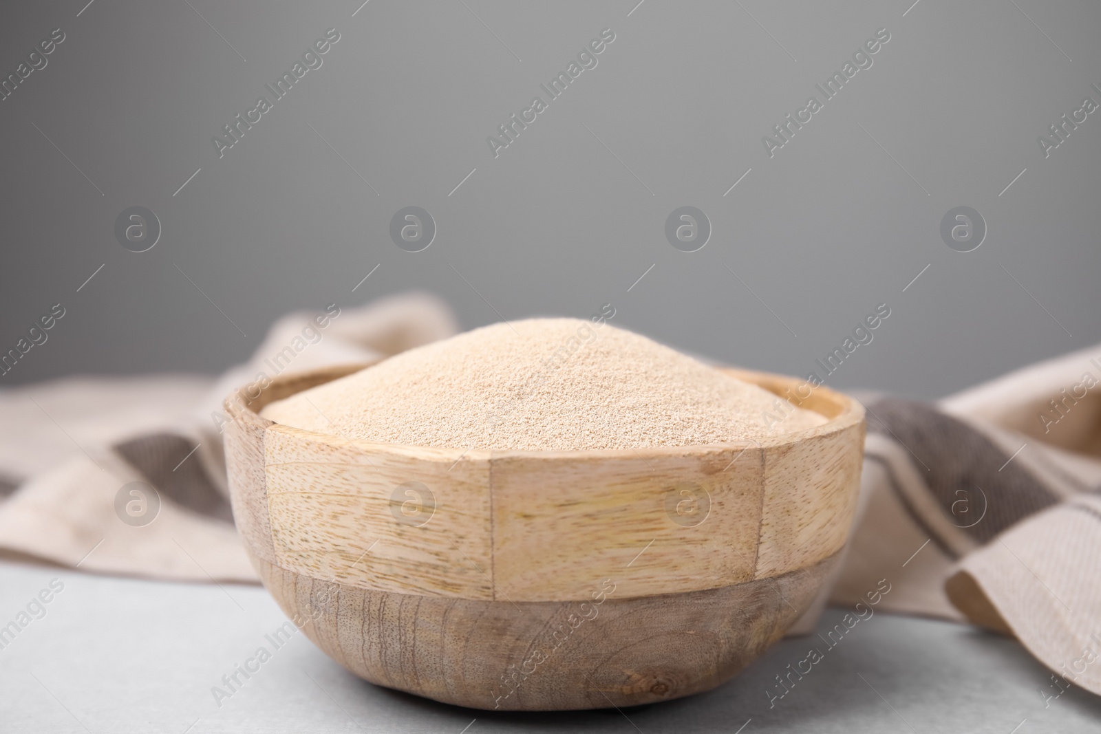 Photo of Granulated yeast in wooden bowl on light gray table, closeup