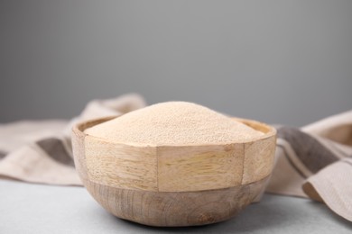 Photo of Granulated yeast in wooden bowl on light gray table, closeup