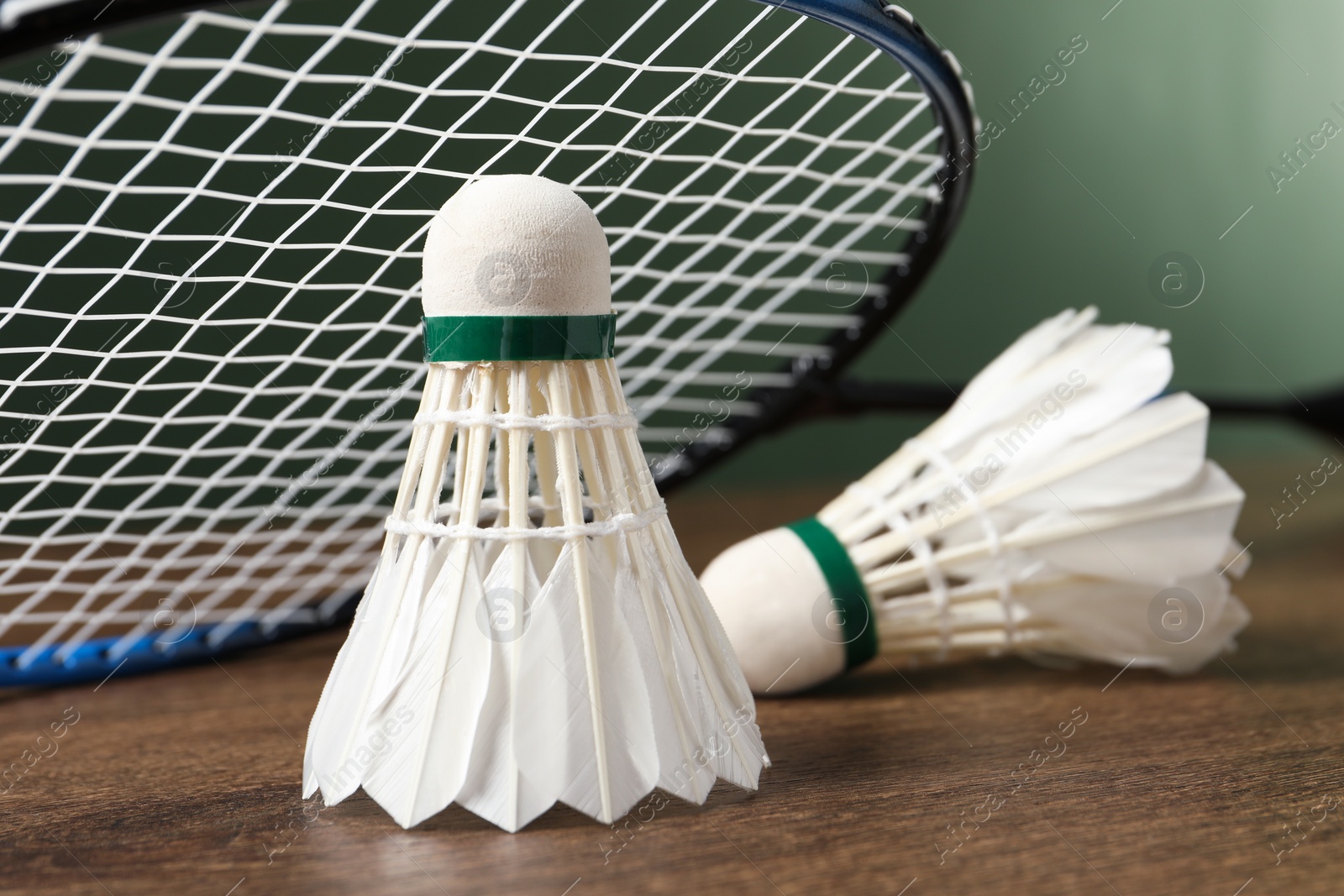 Photo of Feather badminton shuttlecocks and racket on wooden table against green background, closeup. Space for text