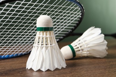 Feather badminton shuttlecocks and racket on wooden table against green background, closeup. Space for text