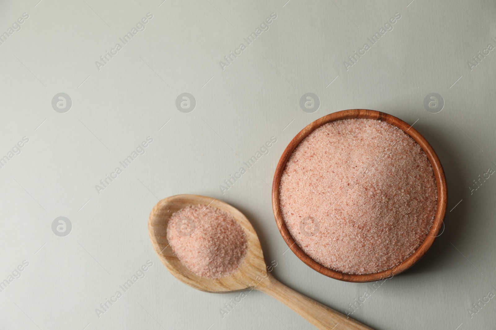 Photo of Himalayan salt in bowl and spoon on grey background, flat lay. Space for text