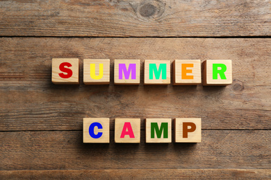 Photo of Phrase SUMMER CAMP made with cubes on wooden background, flat lay
