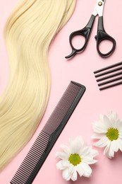 Photo of Hairdresser tools. Blonde hair lock, combs, scissors and flowers on pink background, flat lay