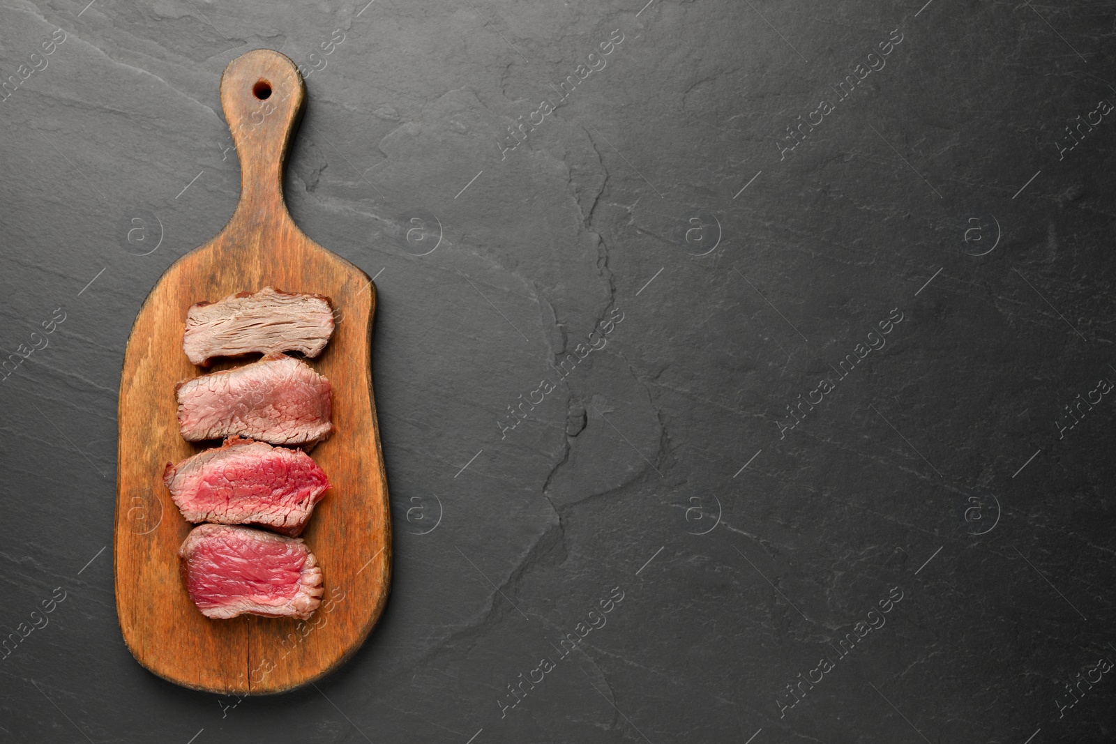 Photo of Delicious sliced beef tenderloin with different degrees of doneness on black table, top view. Space for text