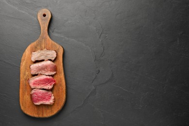 Photo of Delicious sliced beef tenderloin with different degrees of doneness on black table, top view. Space for text