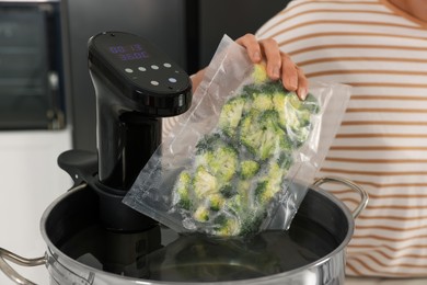 Photo of Woman putting vacuum packed broccoli into pot with sous vide cooker, closeup. Thermal immersion circulator