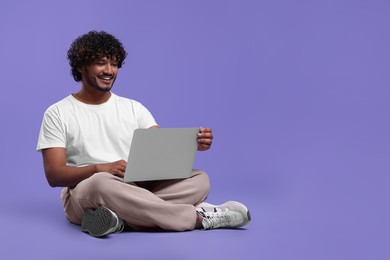 Photo of Happy man with laptop on purple background, space for text