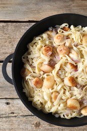 Photo of Delicious scallop pasta with onion in pan on wooden table, top view