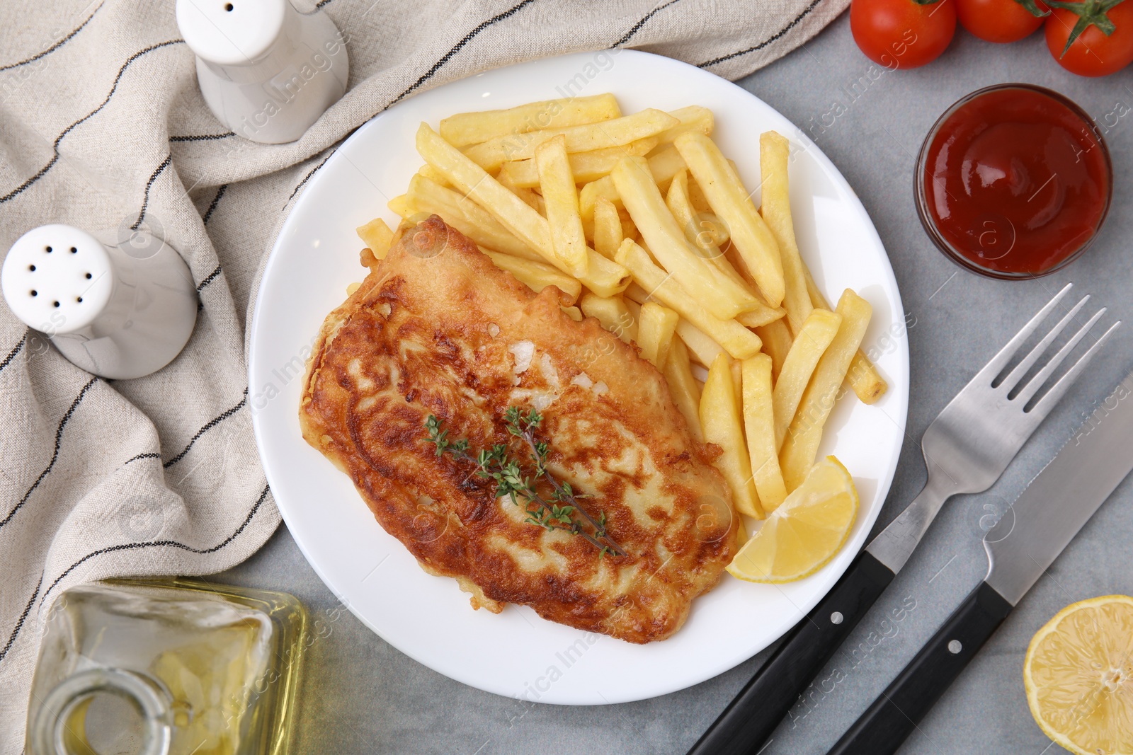 Photo of Tasty soda water battered fish, potato chips and lemon slice served on light grey table, flat lay