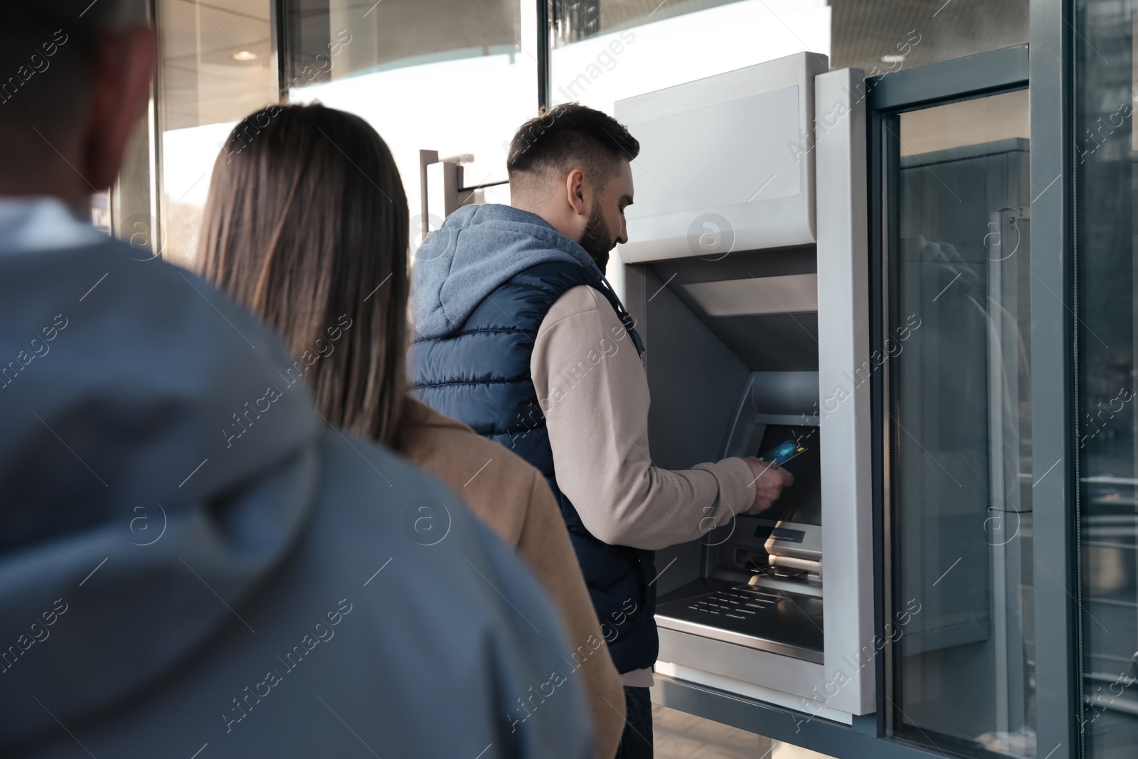 Photo of Young man using cash machine for money withdrawal outdoors. ATM queue