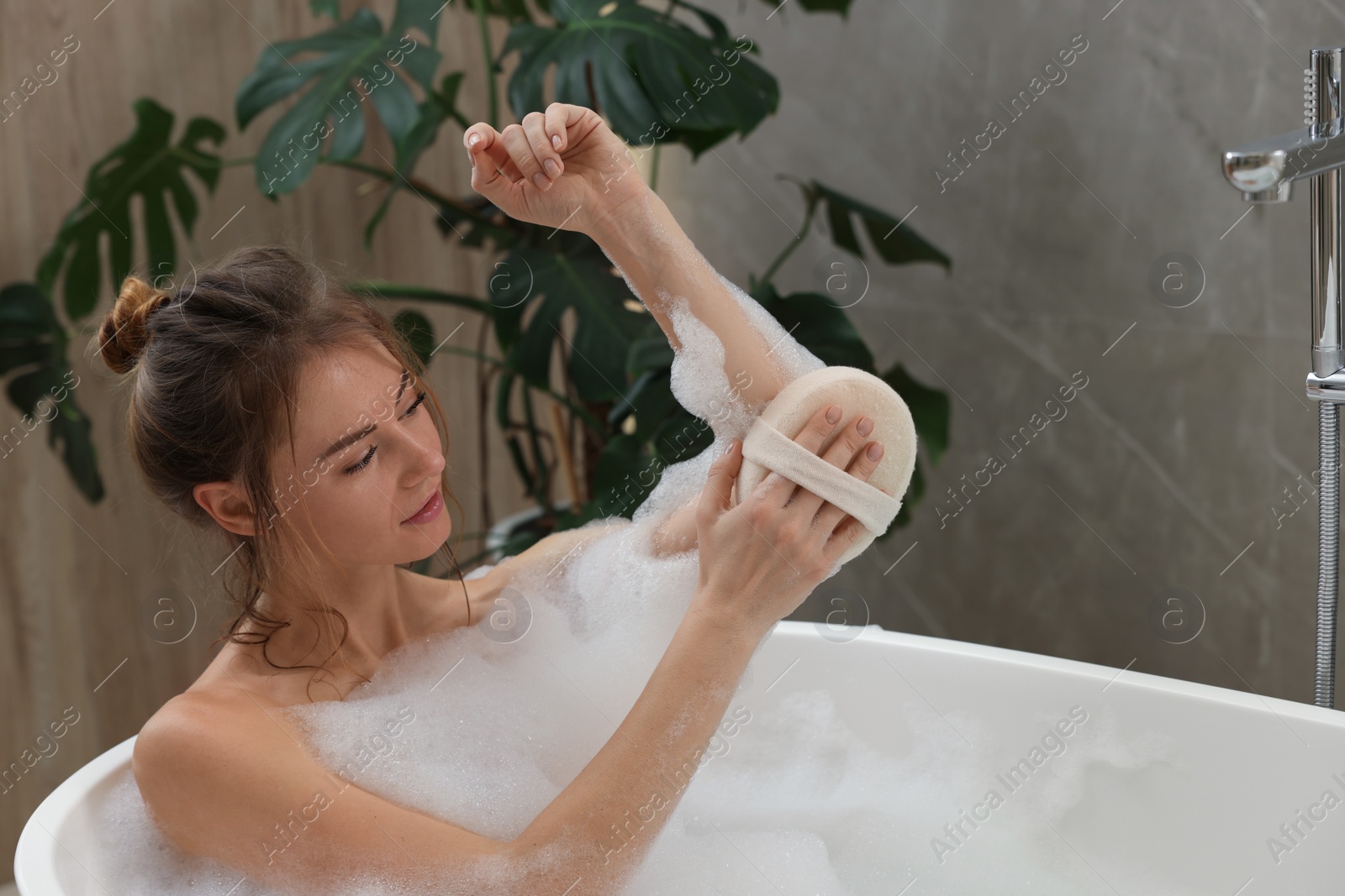 Photo of Beautiful woman with sponge taking bath indoors