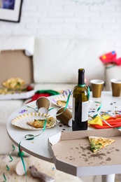 Photo of Messy table with cups, bottle of wine and pizza indoors. Chaos after party